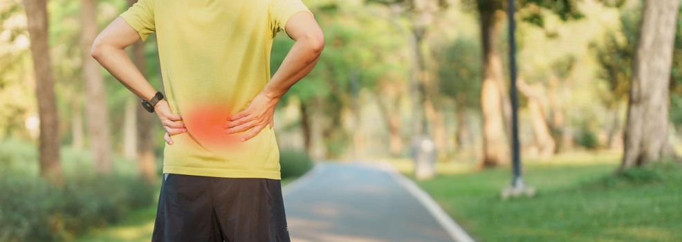 Person holding their lower back while walking outdoors, indicating chronic lower back pain.