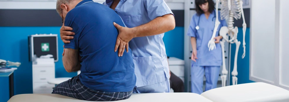Physiotherapist helping an older patient with lower back pain during a clinical assessment.